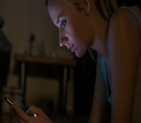 Woman sitting in the dark looking at her phone.