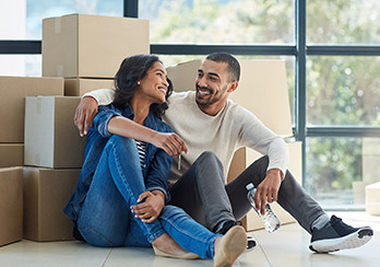 A couple sitting on the floor, leaning up against a pile of moving boxes