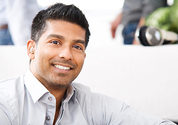 A man in a button-down shirt, smiling and making eye-contact with the camera