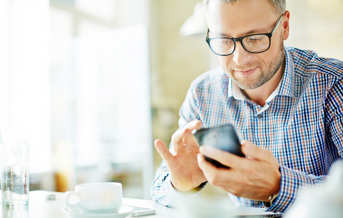 A man holding a smartphone next to coffee
