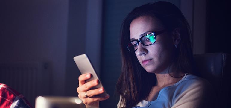Woman sitting in dark room looking at smart phone