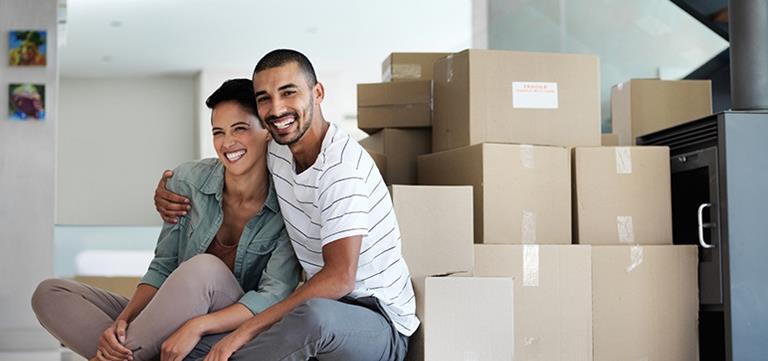 Happy couple sitting on floor in empty room surrounded by cardboard moving boxes