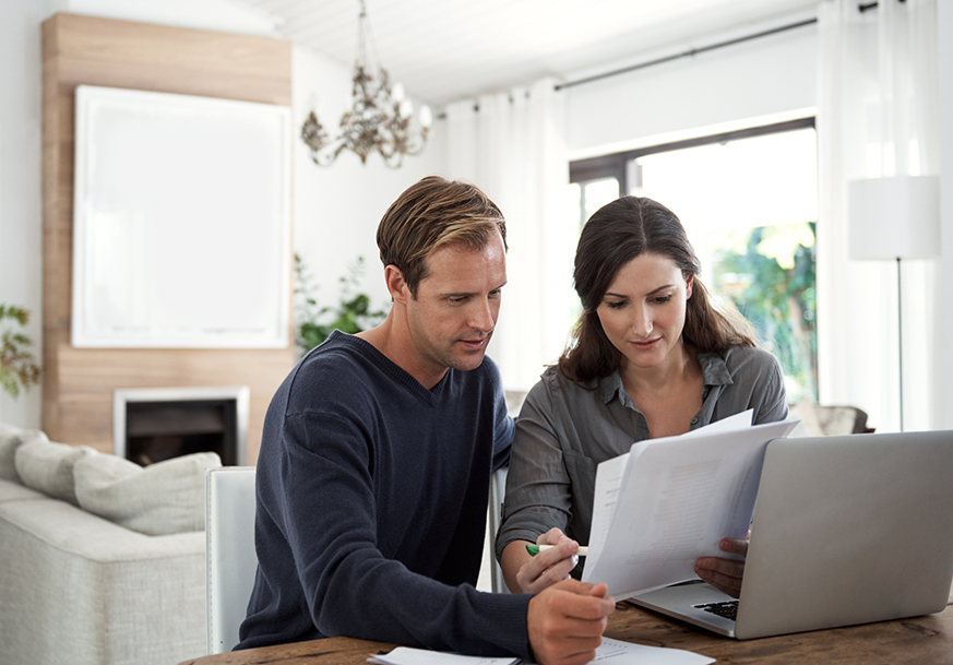 Man and woman sitting at a table, holding and looking at some papers.