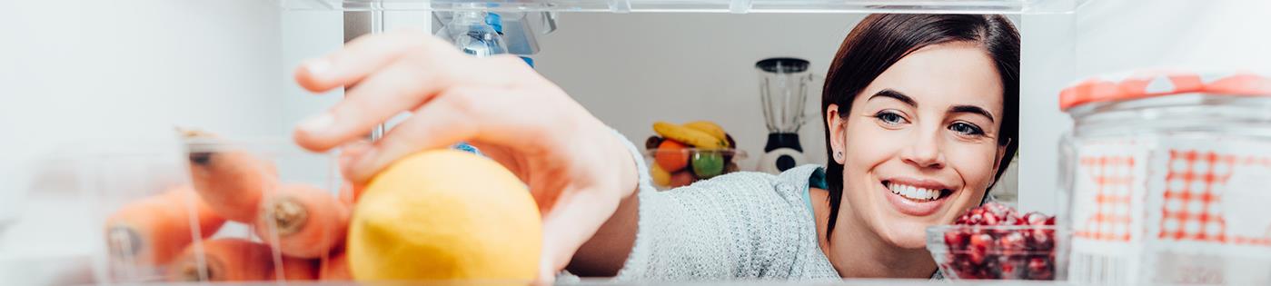 A woman reaching for a lemon inside a refrigerator