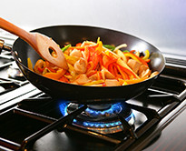 A closeup of vegetables being stirred in a pan atop a burner on a gas stove