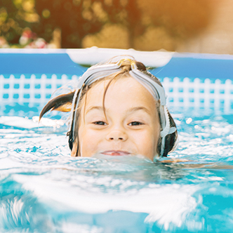 A closeup of a child’s face as she swims in a backyard pool